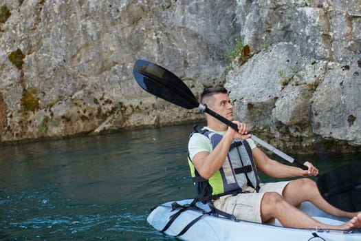 A young man kayaking and exploring a river, surrounded by an impressive natural scenery that exudes an adventurous spirit.