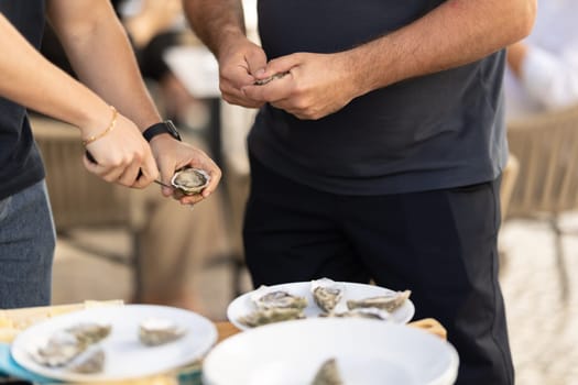 Two men open oysters with a knife at the party. Mid shot