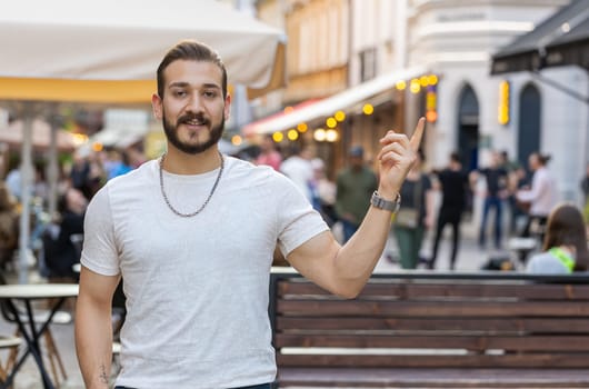 Thoughtful young man showing pointing empty place advertising area for commercial text copy-space for goods promotion. Guy tourist pondering a solution, inspiration dreaming outdoors in city street