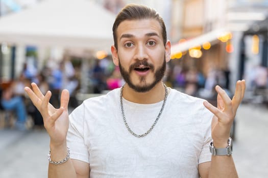 Oh my God, Wow. Bearded young man looking surprised at camera with big open eyes, shocked by sudden victory, game winning, lottery goal achievement, good news outdoors. Guy in city sunshine street