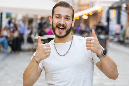 Like. Happy bearded young man looking approvingly at camera showing thumbs up, like sign positive something good positive feedback. Guy walking in urban city sunshine street. Town lifestyles outdoor