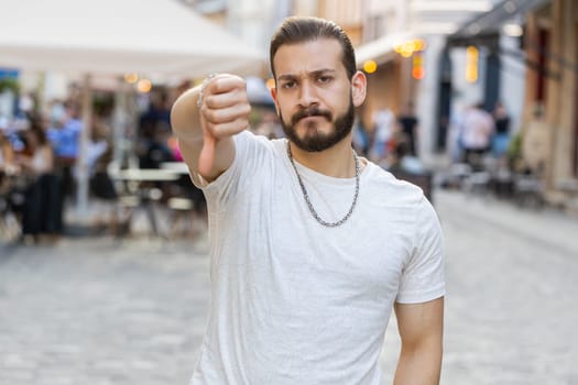 Dislike. Upset bearded young man showing thumbs down sign gesture, expressing discontent, disapproval, dissatisfied bad work, mistake. Displeased guy walking in urban city sunshine street outdoors