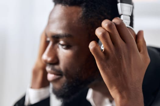 An African-American man sits at his desk in front of his laptop, wearing headphones and chatting on a video call, listening to music. The concept of student business training and online work. High quality photo