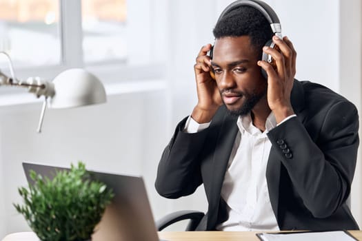 An African-American man sits at his desk in front of his laptop, wearing headphones and chatting on a video call, listening to music. The concept of student business training and online work. High quality photo