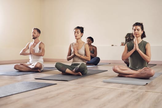 Yoga, meditation and namaste group in a wellness and health class to relax with zen and peace. Female people, spiritual and holistic exercise with calm lotus pose with workout, fitness and gym mat.