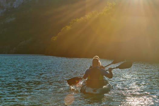 A young couple enjoying an idyllic kayak ride in the middle of a beautiful river surrounded by forest greenery in sunset time.