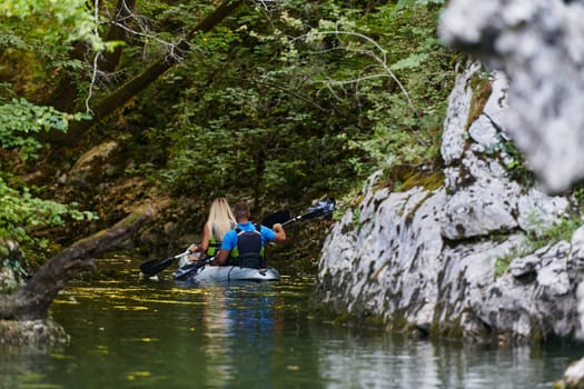 A young couple enjoying an idyllic kayak ride in the middle of a beautiful river surrounded by forest greenery.