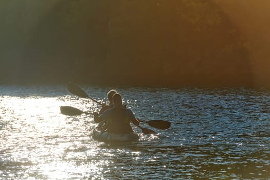 A young couple enjoying an idyllic kayak ride in the middle of a beautiful river surrounded by forest greenery in sunset time.