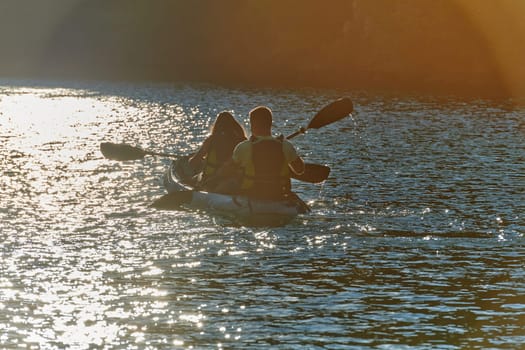 A young couple enjoying an idyllic kayak ride in the middle of a beautiful river surrounded by forest greenery in sunset time.