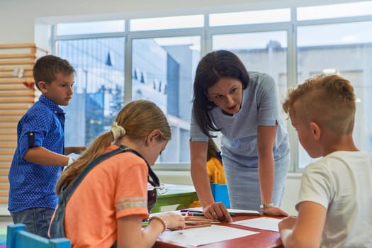 Creative kids during an art class in a daycare center or elementary school classroom drawing with female teacher