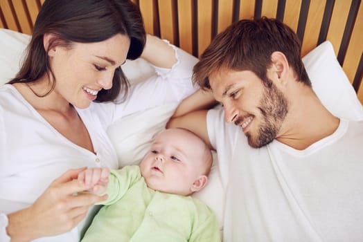 Top view, parents and smile of baby in bedroom for love, care and quality time together at home. Happy mother, father and family relax with cute newborn kid on bed for support, development and joy.