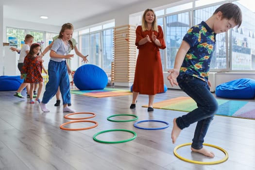 Small nursery school children with female teacher on floor indoors in classroom, doing exercise. Jumping over hula hoop circles track on the floor