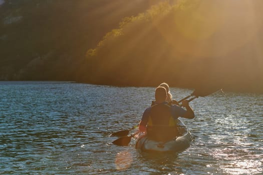 A young couple enjoying an idyllic kayak ride in the middle of a beautiful river surrounded by forest greenery in sunset time.