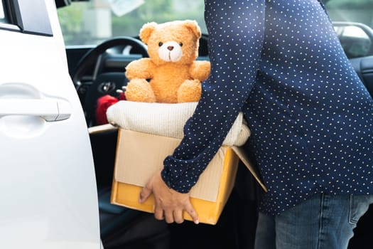 Volunteer woman provide clothing donation box with used clothes and doll in car to support help for refugee, homeless or poor people in the world.