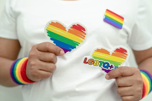 Asian lady wearing rainbow flag wristbands and hold heart, symbol of LGBT pride month celebrate annual in June social of gay, lesbian, bisexual, transgender, human rights.