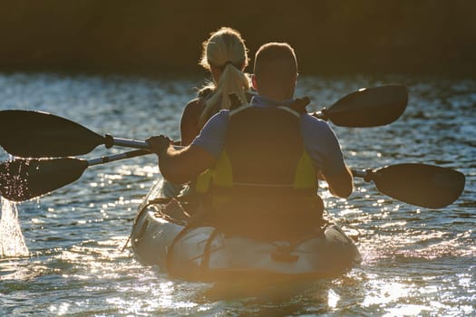 A young couple enjoying an idyllic kayak ride in the middle of a beautiful river surrounded by forest greenery in sunset time.