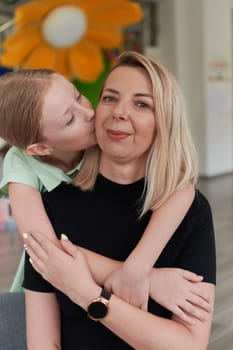 A cute little girl kisses and hugs her mother in preschool. High quality photo