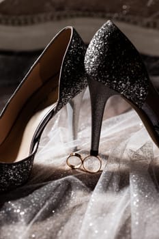 Golden rings of the newlyweds between white shoes with heels. Precious rings of the bride and groom
