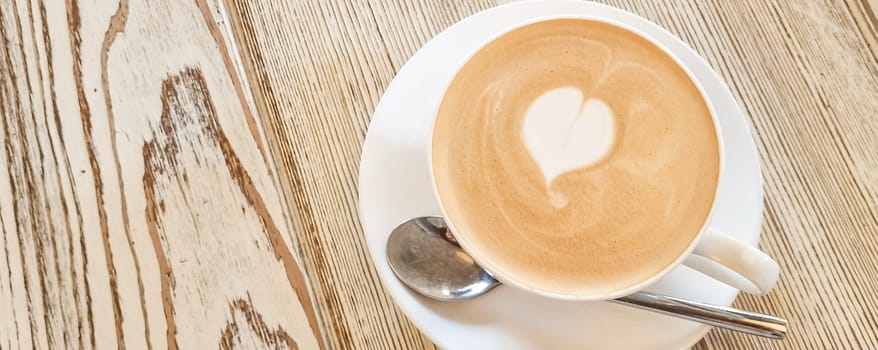 Two cups of cappuccino with latte art on wooden background. Beautiful foam, greenery ceramic cups, stylish toning, place for text.