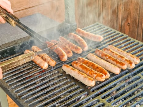 Fresh sausage and hot dogs grilling outdoors on a gas barbecue grill.