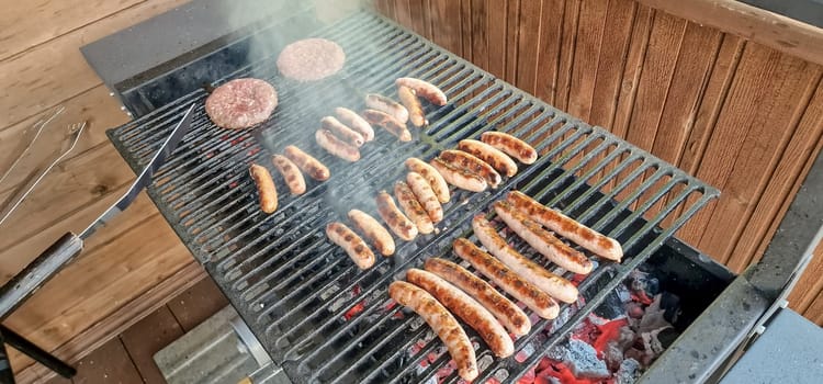 Fresh sausage and hot dogs grilling outdoors on a gas barbecue grill.