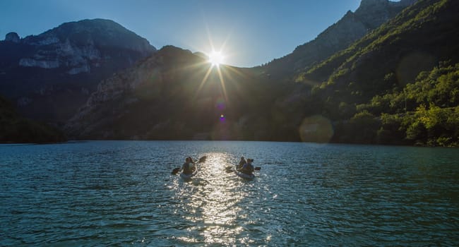 A group of friends enjoying fun and kayaking exploring the calm river, surrounding forest and large natural river canyons during an idyllic sunset