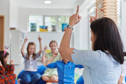 A happy female teacher sitting and playing hand games with a group of little schoolchildren.