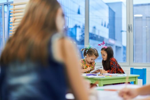 Creative kids during an art class in a daycare center or elementary school classroom drawing with female teacher