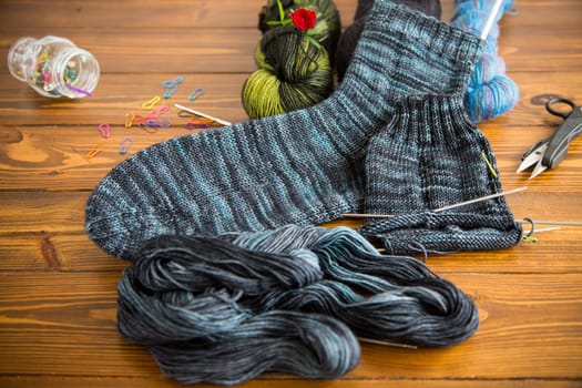 Set for hand knitting warm winter socks made of natural woolen yarn, on a wooden table.