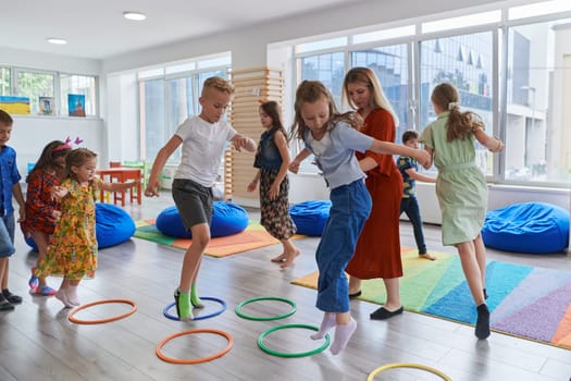 Small nursery school children with female teacher on floor indoors in classroom, doing exercise. Jumping over hula hoop circles track on the floor