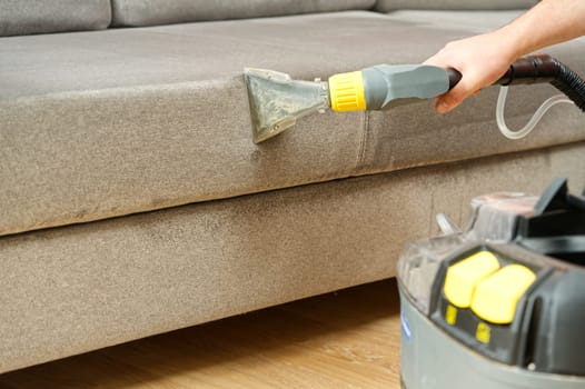 Dry cleaner's man employee removing dirt from furniture in flat, closeup, vacuum clean sofa with professional equipment. cleaning sofa with washing suction cleaner closeup.