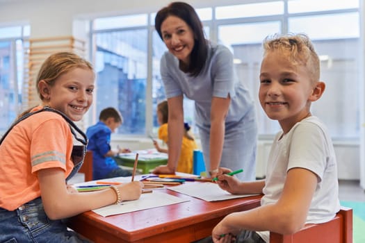 Creative kids during an art class in a daycare center or elementary school classroom drawing with female teacher