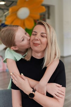 A cute little girl kisses and hugs her mother in preschool. High quality photo