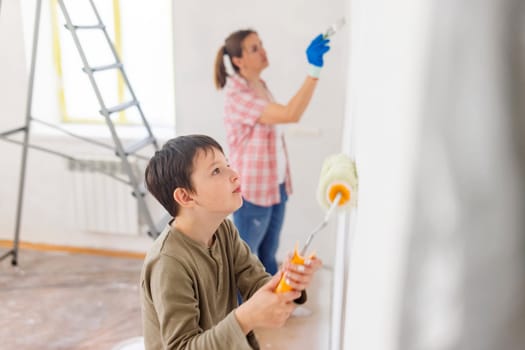 Happy family mother and child son paint the wall with paint using roller and brush. Repair in the apartment