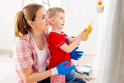 Happy family mother and child son paint the wall with paint using roller and brush. Repair in the apartment