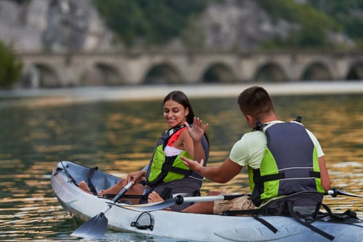 A young couple enjoying an idyllic kayak ride in the middle of a beautiful river surrounded by forest greenery.