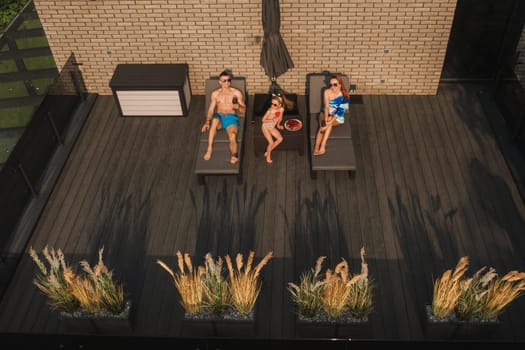 A happy family in swimsuits sunbathe in summer on their terrace on sun beds.