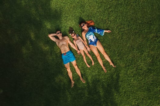 Top view of a happy family in swimsuits lying on the green grass.