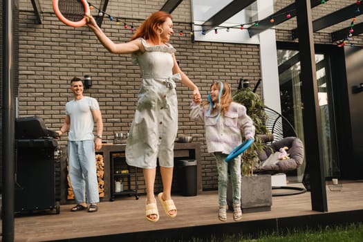 A happy family is resting not far from their home. dad is cooking a barbecue, and mom and daughter are playing jumping.