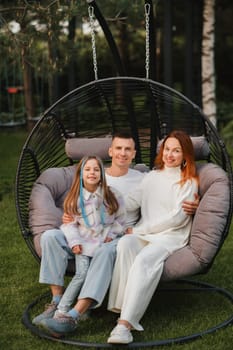 A happy family is sitting in a hammock on the lawn near the house.