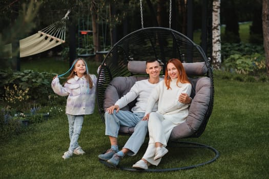 A happy family is sitting in a hammock on the lawn near the house.