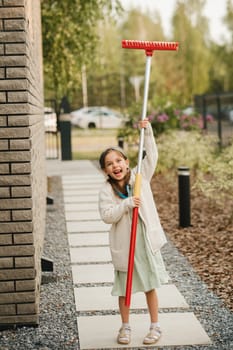 A little girl with a brush cleans a path on the street in the courtyard.