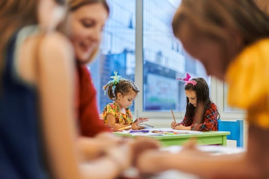 Creative kids during an art class in a daycare center or elementary school classroom drawing with female teacher