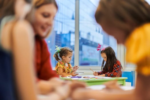 Creative kids during an art class in a daycare center or elementary school classroom drawing with female teacher