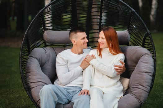 A happy family is sitting in a hammock on the lawn near the house.