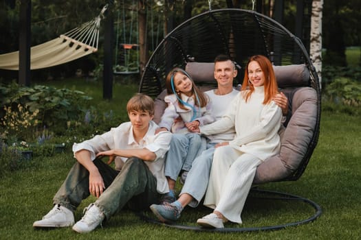 A happy family is sitting in a hammock on the lawn near the house.