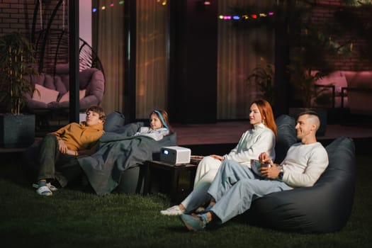 family mother, father and children watch a projector, movies with popcorn in the evening in the courtyard.