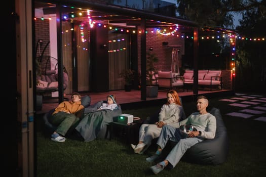 family mother, father and children watch a projector, movies with popcorn in the evening in the courtyard.