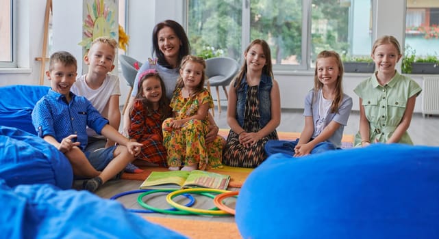 A happy female teacher sitting and playing hand games with a group of little schoolchildren.