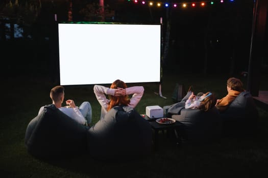 family mother, father and children watch a projector, movies with popcorn in the evening in the courtyard